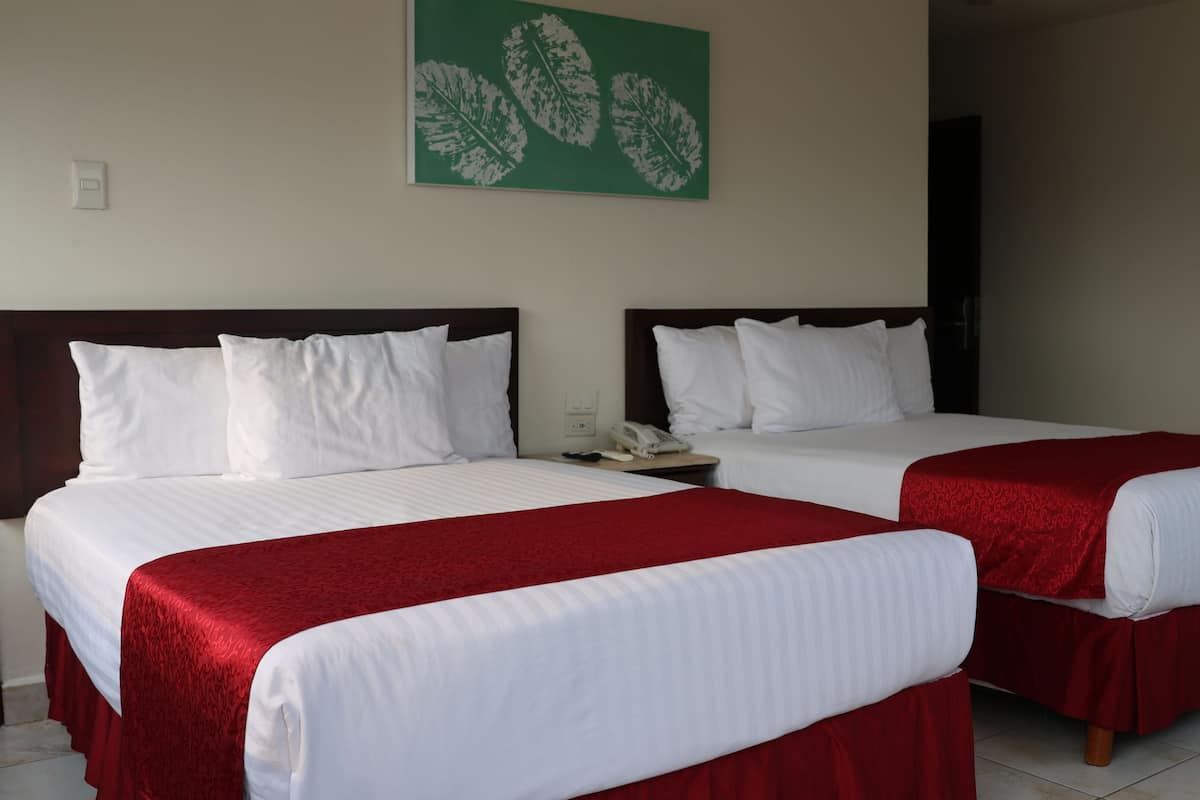 Two single beds with white linens and red bedspreads, a green leaf artwork on the wall, and a small bedside table with a phone.