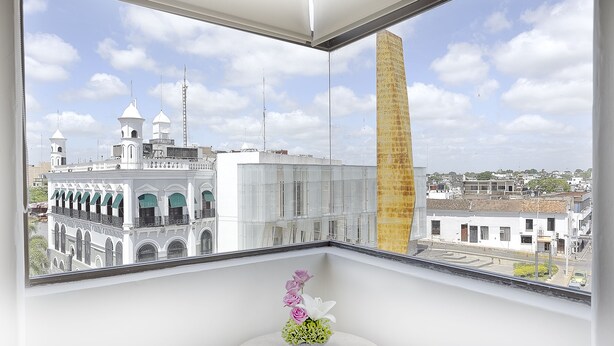 A room with a large window overlooking a historic building with multiple towers and a tall chimney.