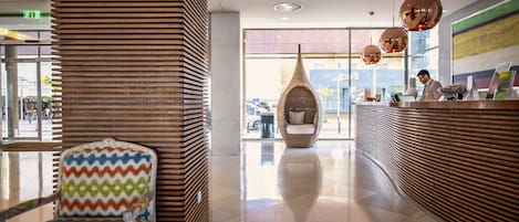 A modern lobby with a reception desk, a wicker chair, and a patterned armchair.