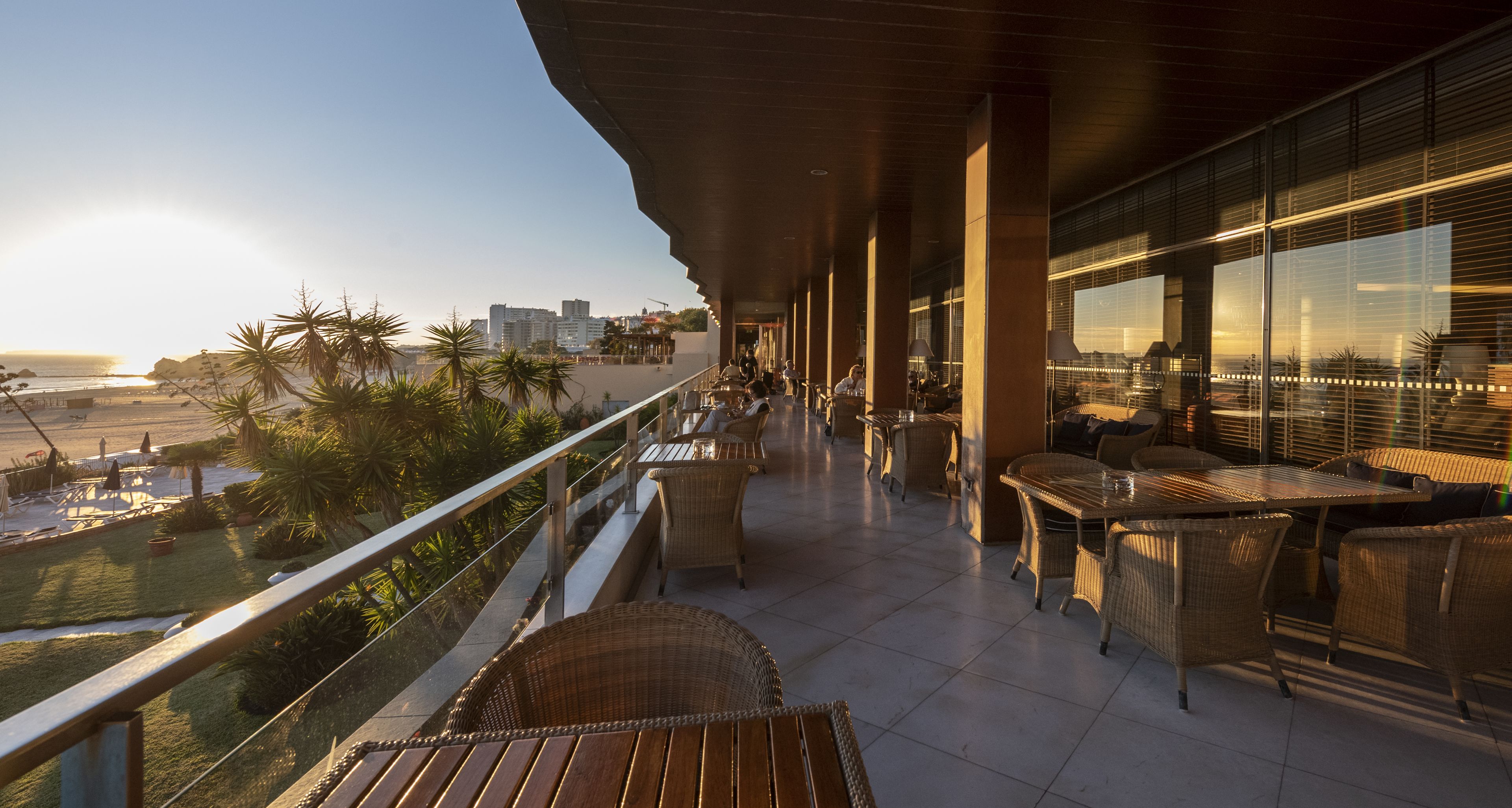Ein Balkon mit Korbmöbeln, Blick auf den Strand und eine Stadtlandschaft im Hintergrund.