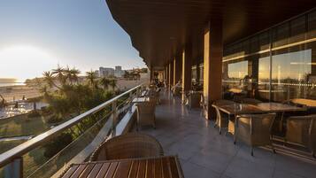 A balcony with wicker furniture, a view of the beach, and a cityscape in the background.