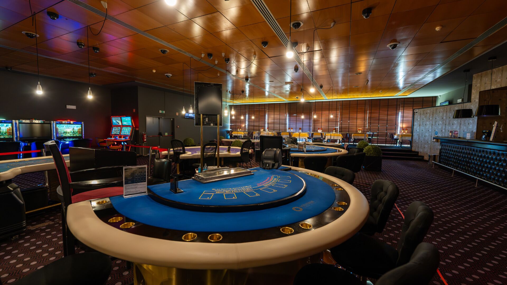 A casino with multiple gaming tables, including a prominent blackjack table, and a bar area with a counter and seating.