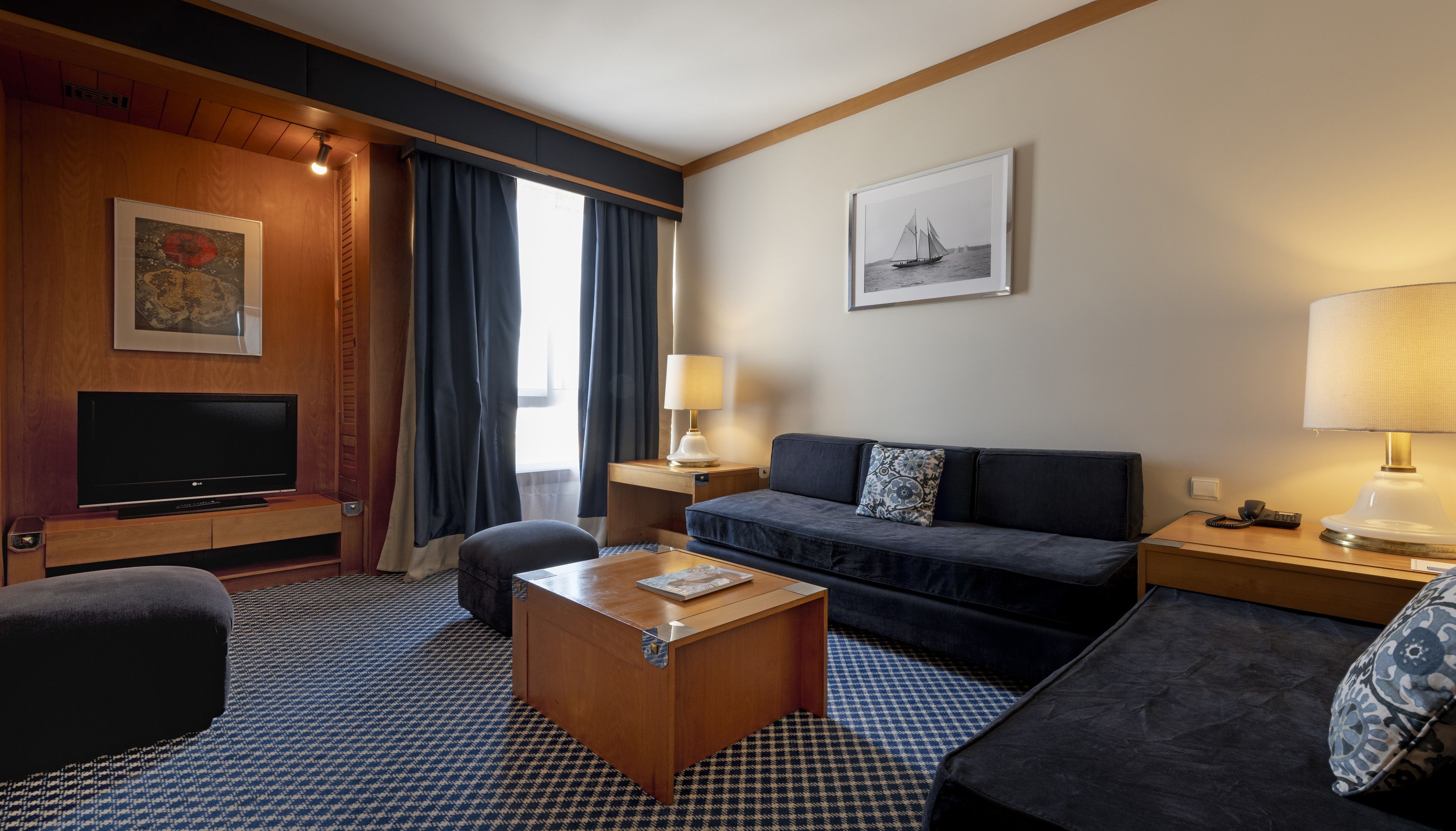 A hotel room with a flat-screen TV, a sofa, a coffee table, a desk, and a lamp.