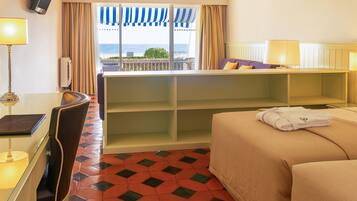 Une chambre d’hôtel avec un lit, un bureau, une chaise, une petite table et une vue sur la mer.