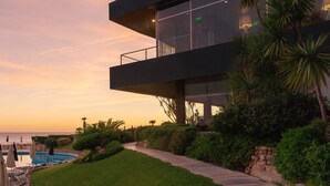 A modern building with a pool, surrounded by greenery and overlooking a body of water.