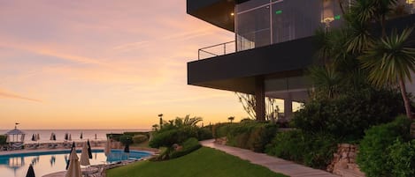 Ein modernes Gebäude mit Pool, umgeben von Grünflächen und mit Blick auf ein Gewässer.