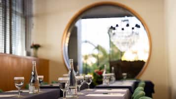 Una mesa de comedor con copas y botellas de vino, un espejo que refleja un candelabro, y vistas a zonas verdes al exterior.