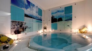 A spa room with a hot tub, framed artwork, candles, and towels.