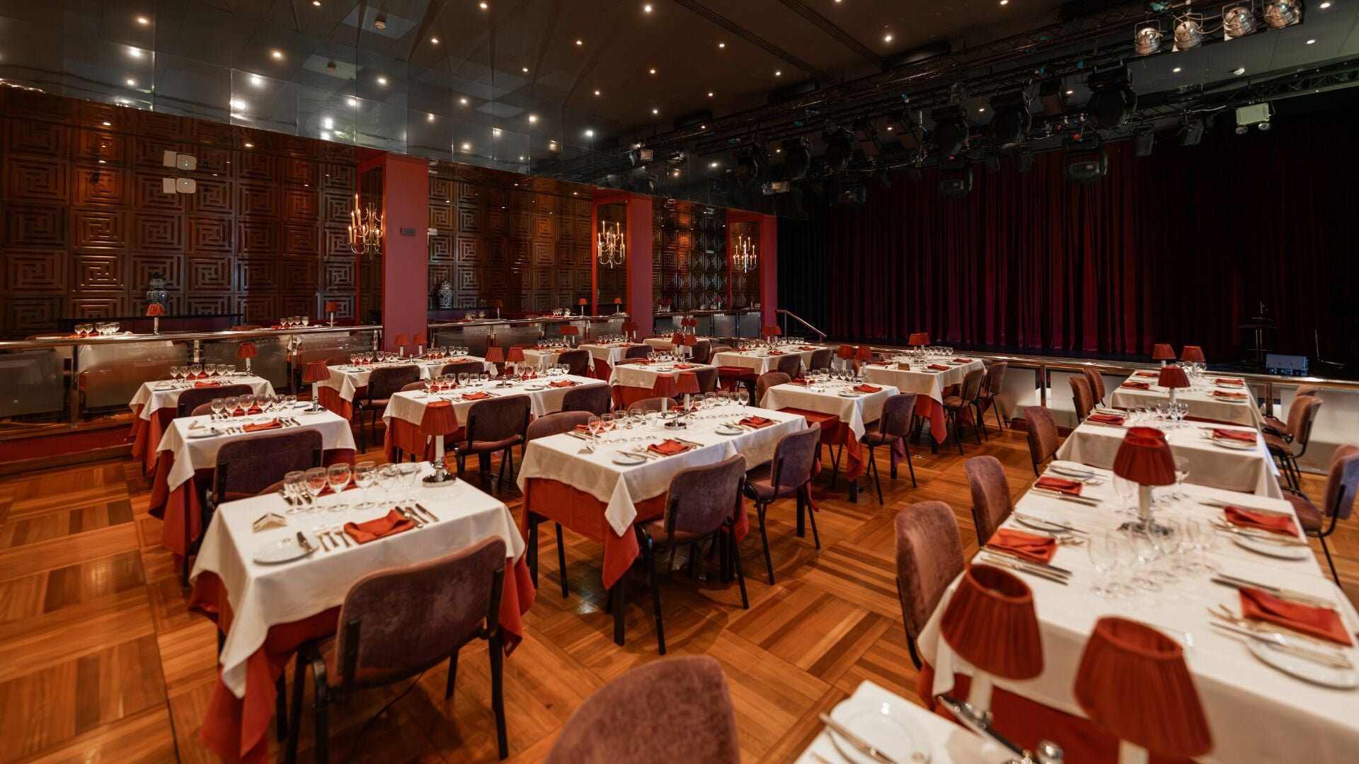 Un amplio salón de banquetes con varias mesas redondas dispuestas para comer, con manteles blancos y servilletas rojas.