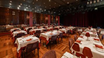 A large banquet hall with multiple round tables set for dining, featuring white tablecloths and red napkins.