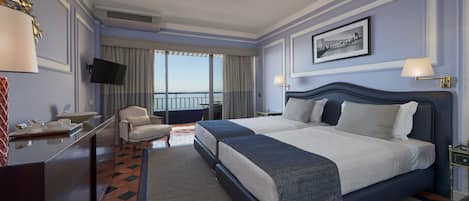 A hotel room with a large bed, a desk with a chair, a TV, and a balcony with a view.