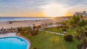A resort with a swimming pool, beach access, and a view of the sunset over the ocean.