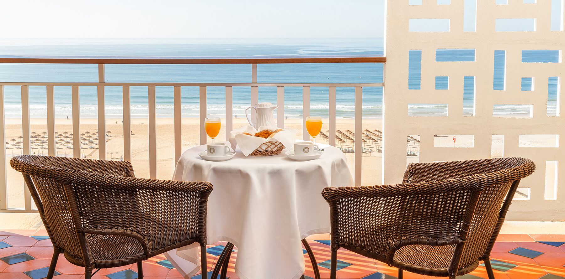 A balcony with wicker chairs, a table with a white tablecloth, and a view of the beach and ocean.