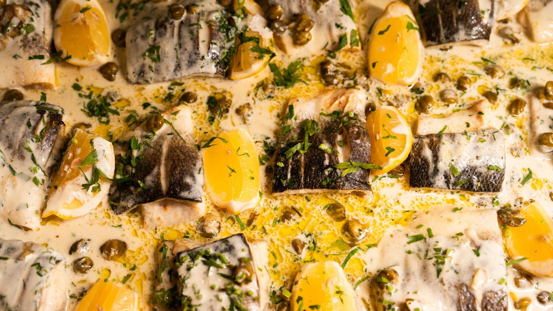A dish with fish, lemon slices, capers, and herbs.