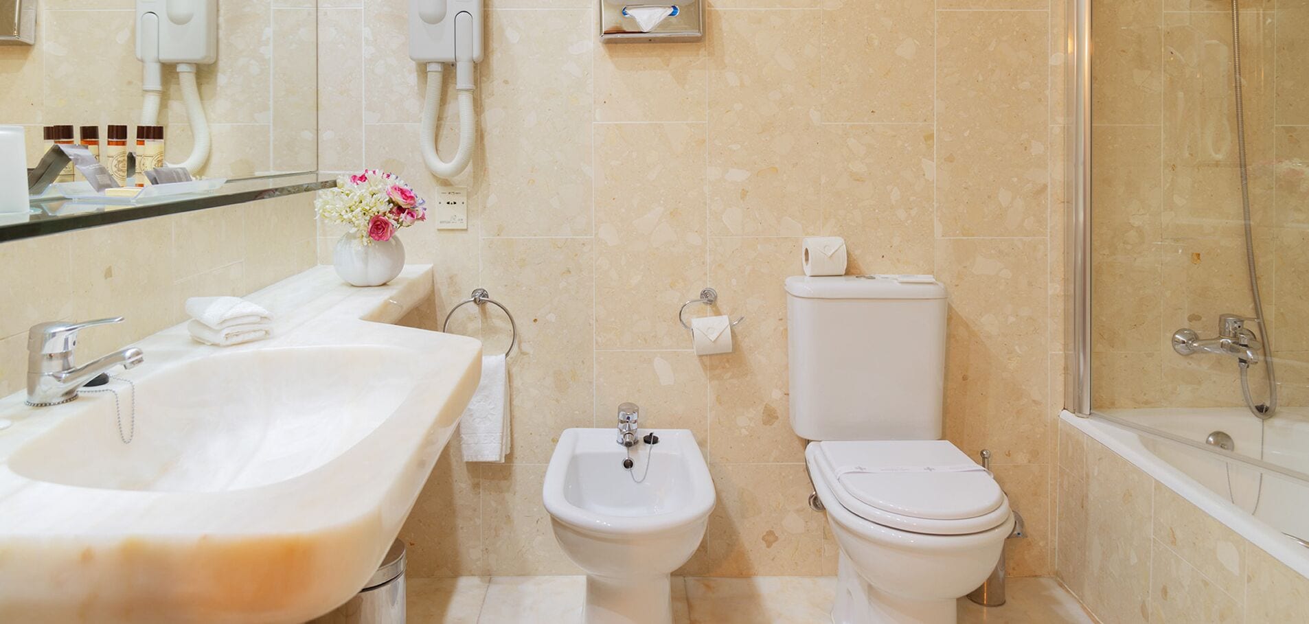 A bathroom with a large sink, bidet, toilet, and a glass-enclosed shower.