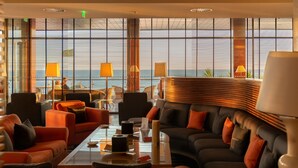 A modern lounge area with a large window offering a view of the sea and ships. There are multiple seating options including sofas and chairs.