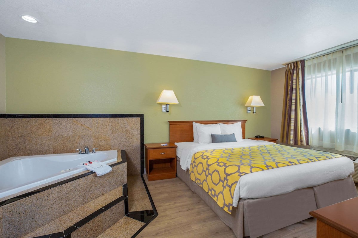 Habitación de hotel con una bañera grande, una cama con colcha estampada, dos lámparas de noche y una mesita de noche.