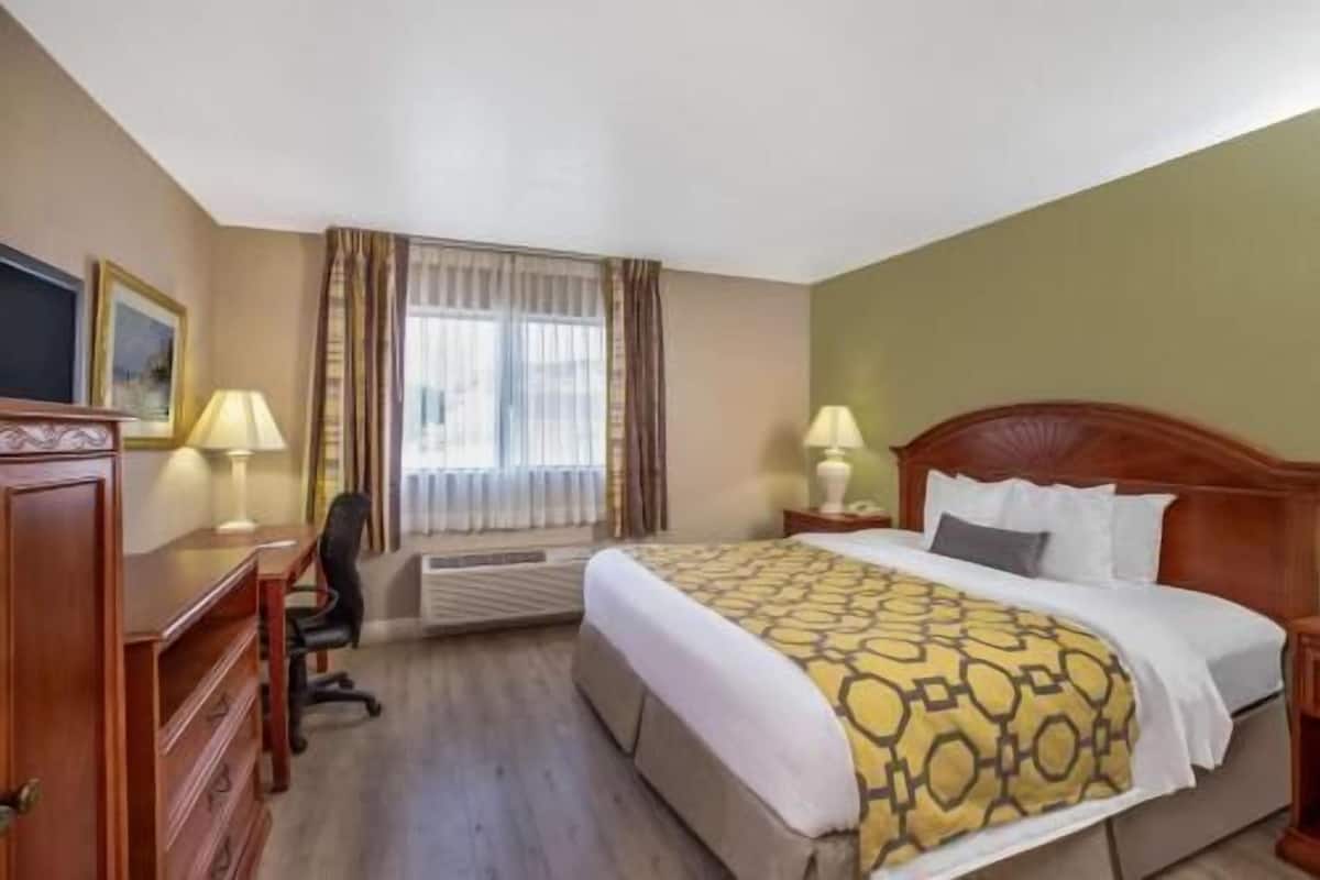 Habitación de hotel con cama, dos lámparas de noche, un escritorio con silla y una ventana con cortinas.