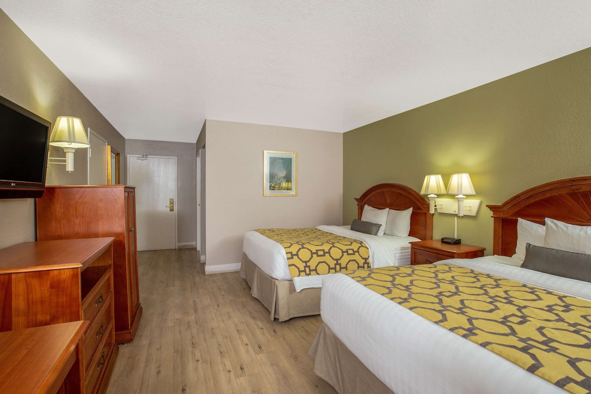 Habitación de hotel con dos camas, televisor, muebles de madera y un cuadro en la pared.