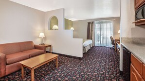 Habitación de hotel con sofá, una mesita, cama, escritorio y kitchenette.