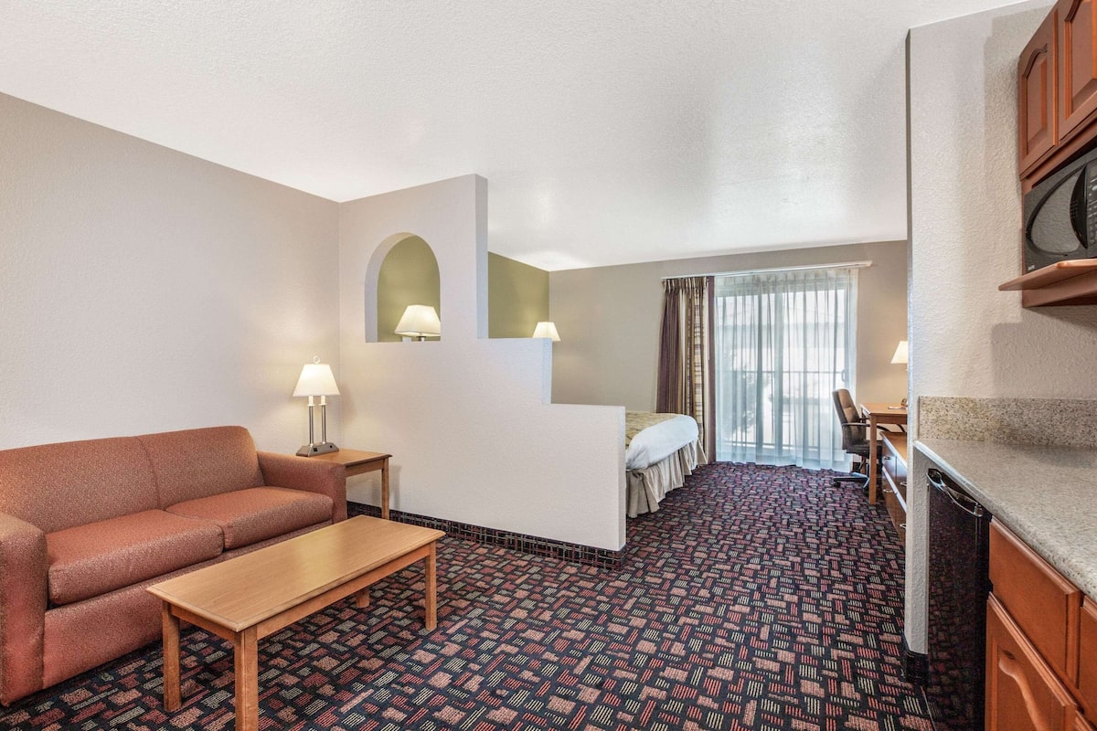 Habitación de hotel con sofá, una mesita, cama, escritorio y kitchenette.