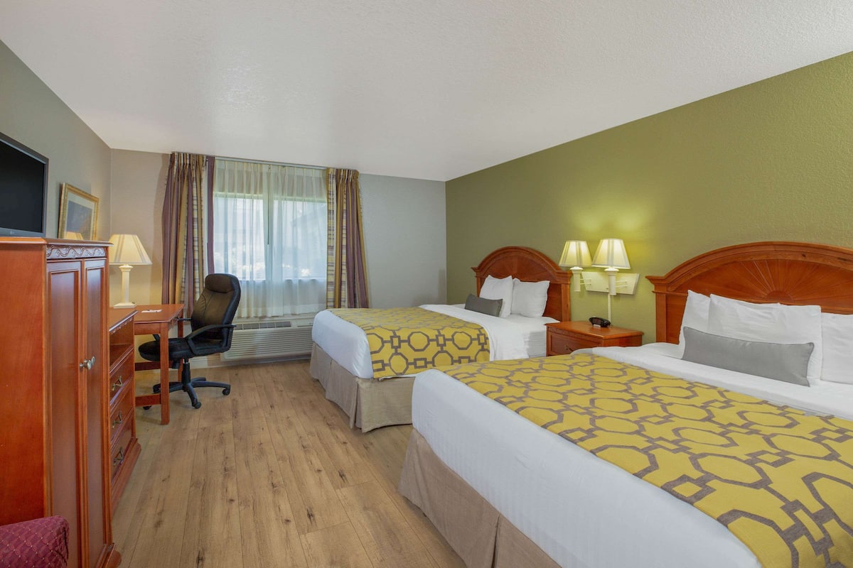Habitación de hotel con dos camas, un escritorio, una silla y un televisor.