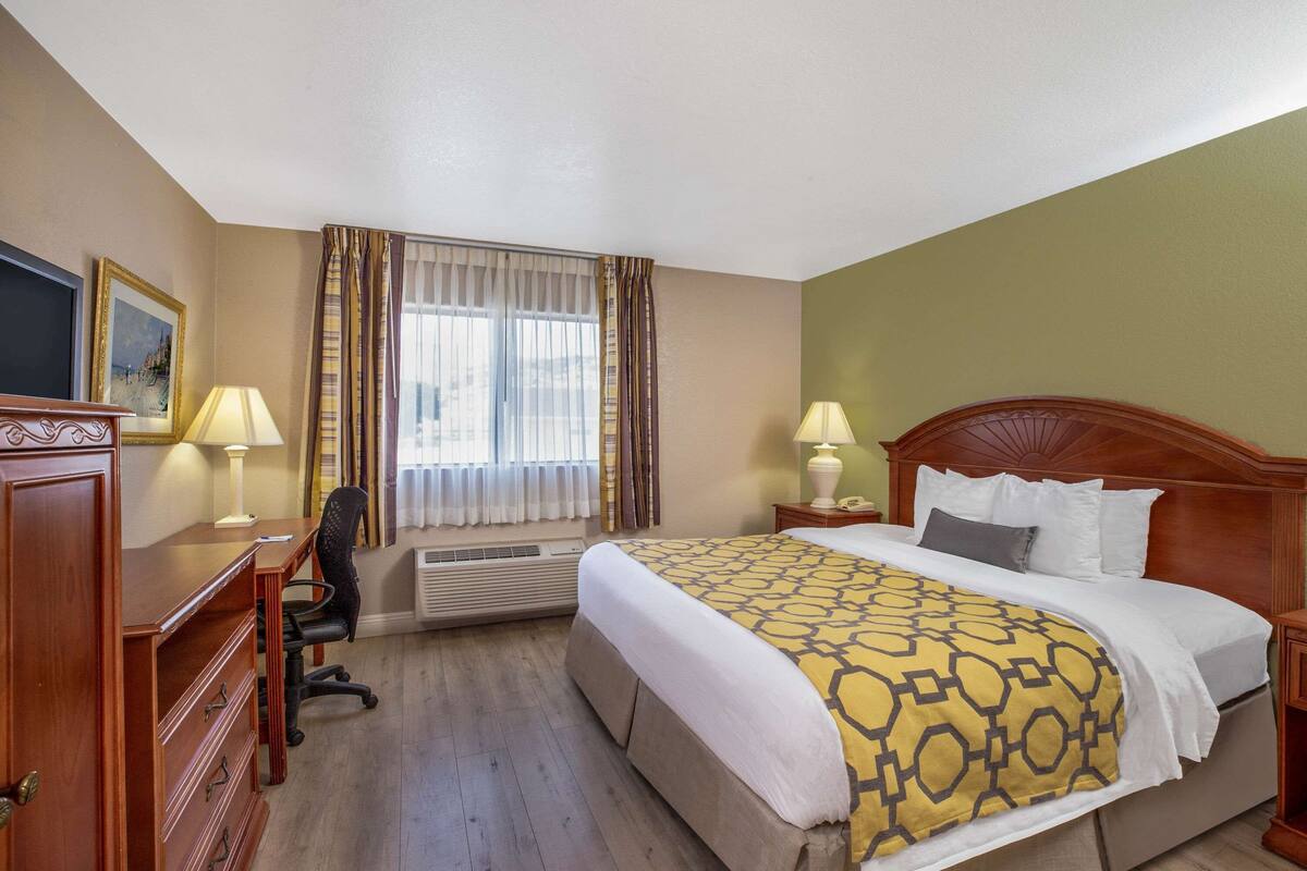 Una habitación de hotel con cama, escritorio, silla y dos lámparas.