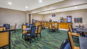 Un comedor de hotel con varias mesas y sillas, una barra de desayuno y una estación de café.