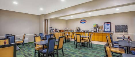 Un comedor de hotel con varias mesas y sillas, una barra de desayuno y una estación de café.