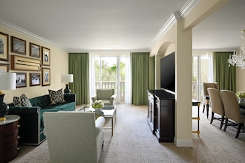 A hotel room with a bed, a desk, a green sofa, a chair, a mirror, a framed picture, and a balcony with a view. at Trump National Doral Miami
