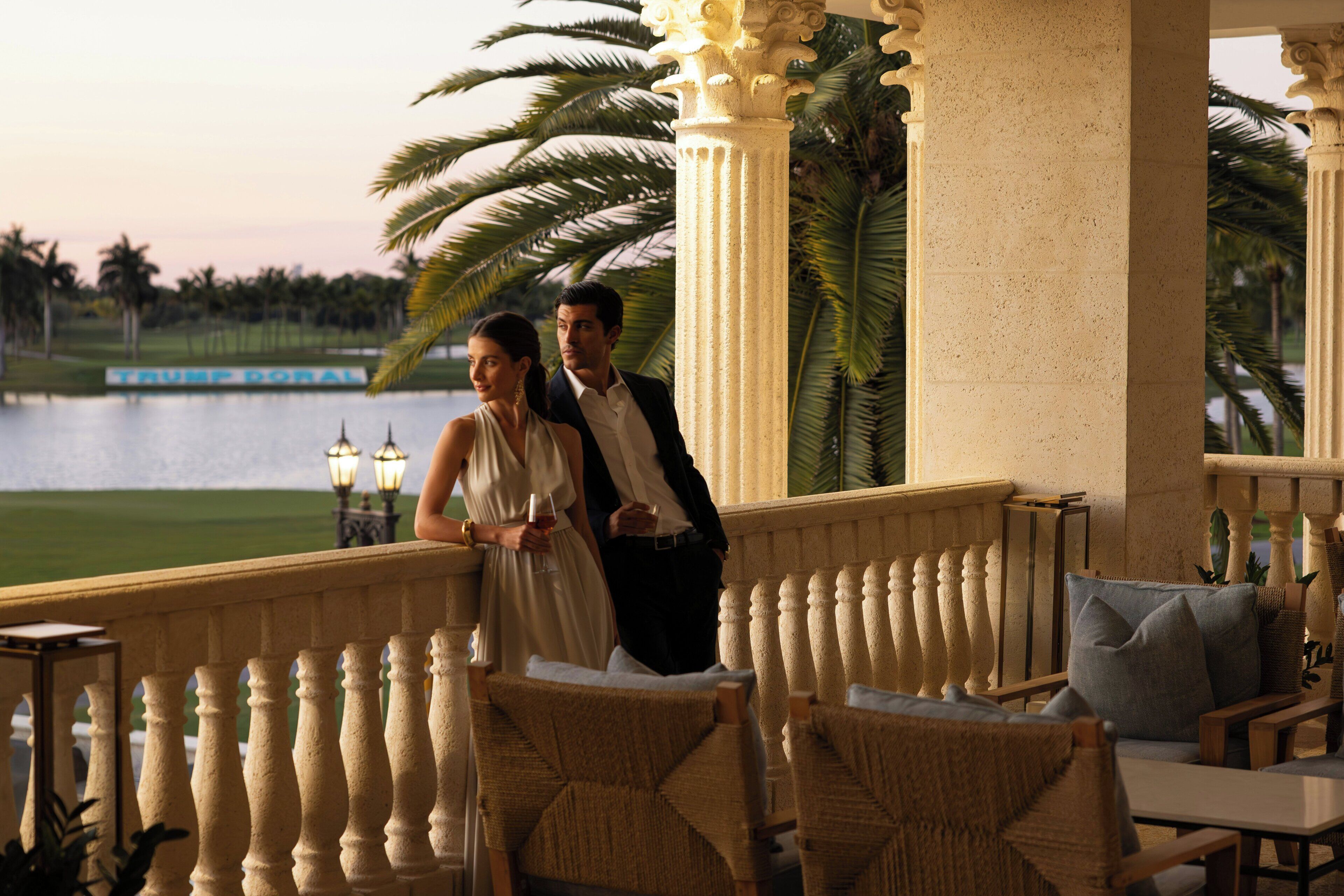 A balcony with wicker furniture, a view of a lake, and palm trees.