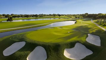 A golf course with sand bunkers, water hazards, and a clear sky.