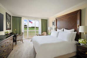 A hotel room with a large bed, a desk, a chair, a dresser, and a view of a golf course. - Trump National Doral Miami (Miami)