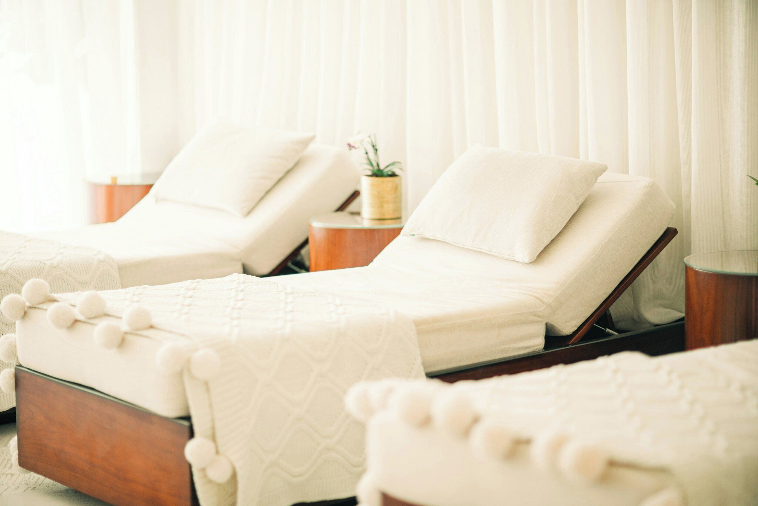 A room with two reclining chairs, a bedside table with a plant, and a window with curtains.