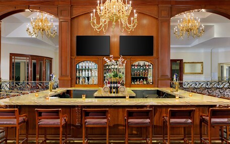 A bar area with a marble counter, multiple chairs, and a large chandelier.