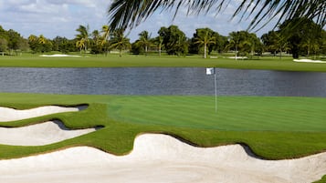 Un parcours de golf avec des bunkers de sable, un obstacle d’eau et des palmiers.