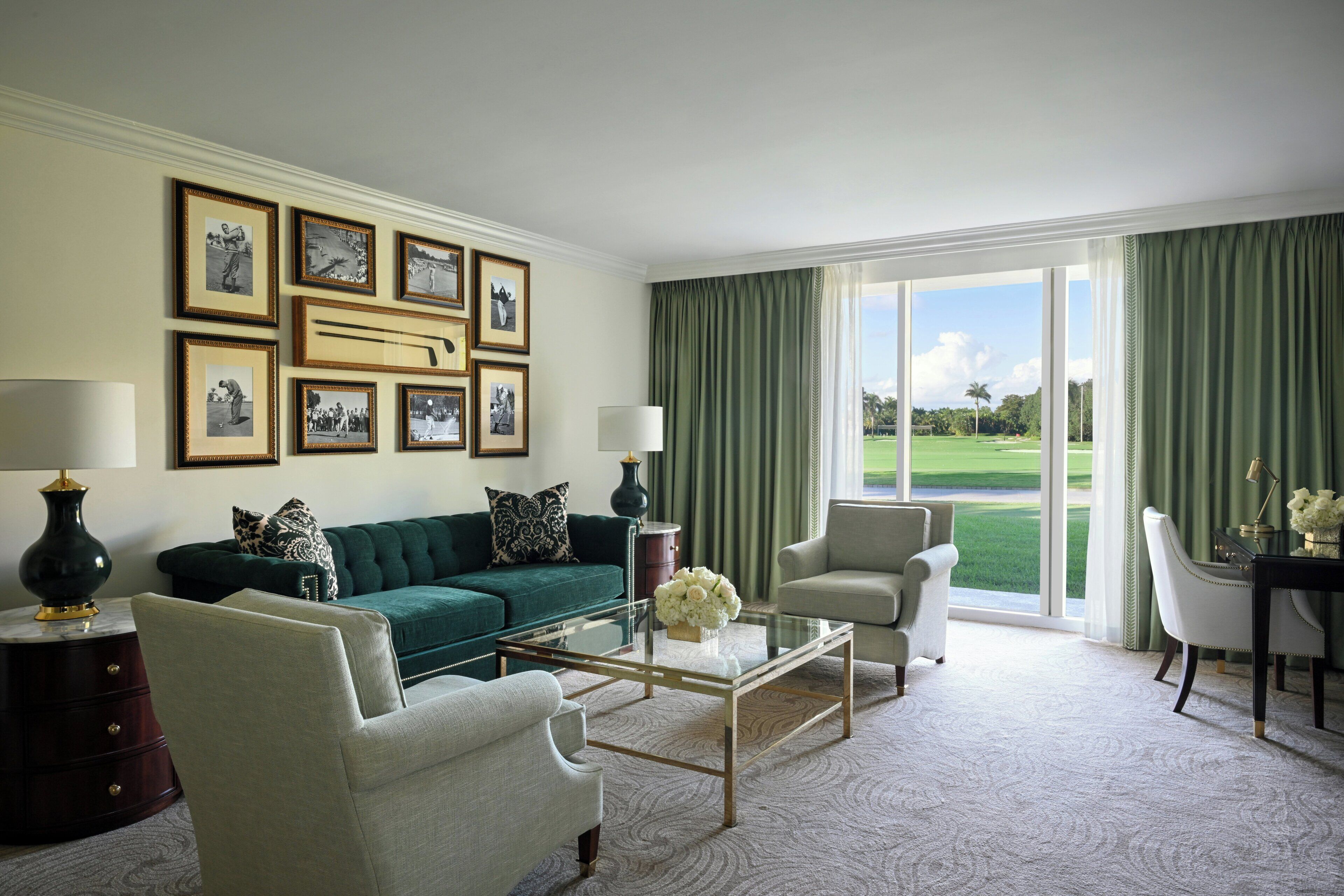 A living room with a green sofa, two armchairs, a glass coffee table, and a view of a golf course through large windows.