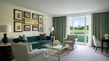 A living room with a green sofa, two armchairs, a glass coffee table, and a view of a golf course through large windows.