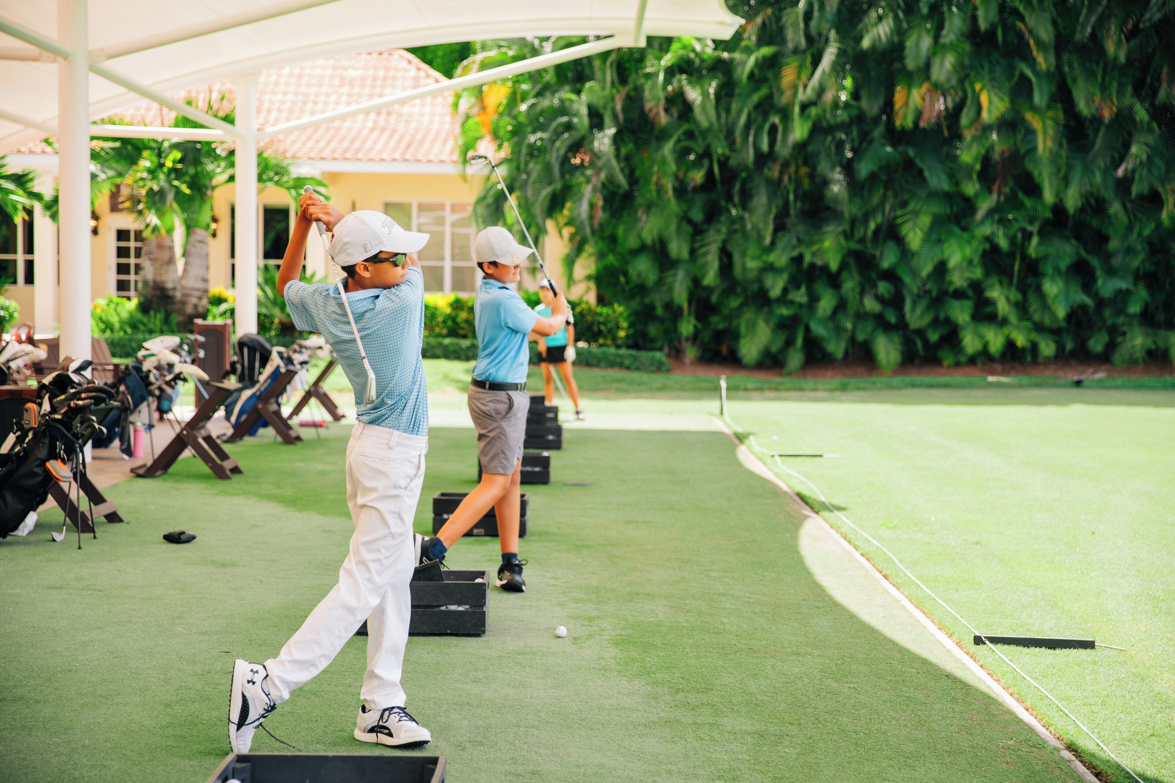 A golf course with players in motion, a clear sky, and lush greenery.