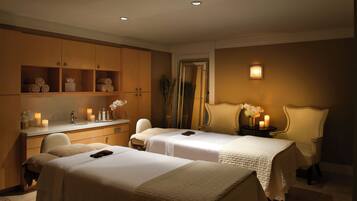 Une chambre d’hôtel avec deux lits, une coiffeuse avec un miroir et une petite table décorée de bougies et de fleurs.