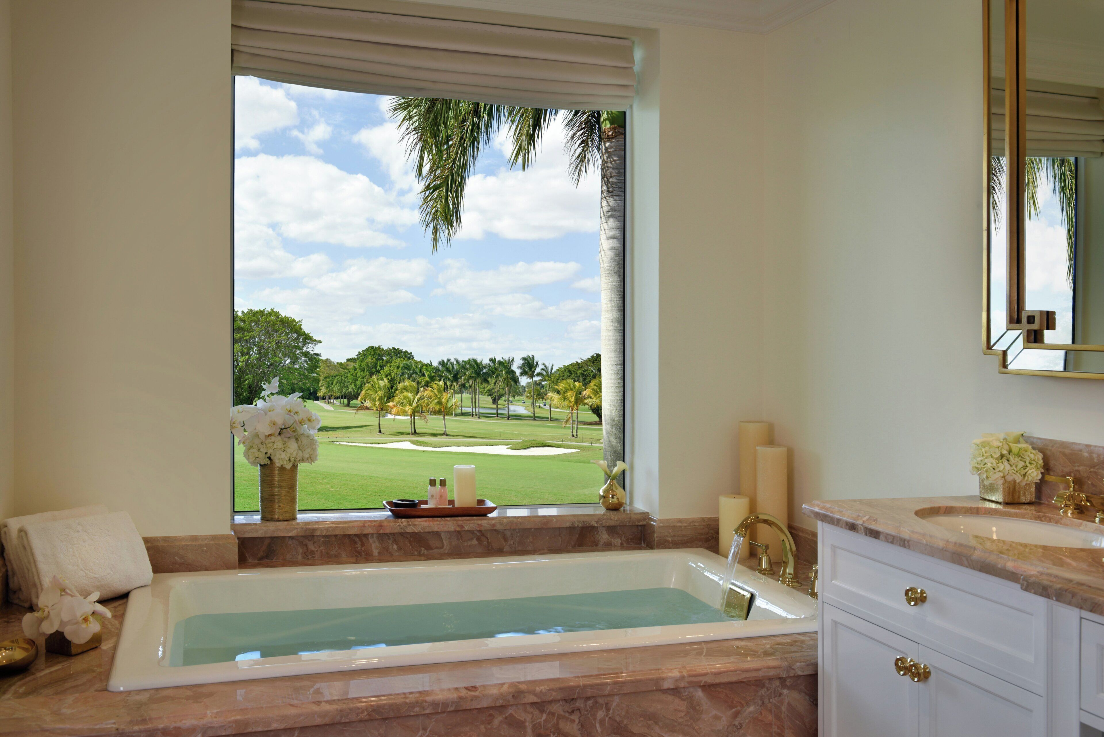 A bathroom with a bathtub, a window with a view of a golf course, and a vanity with a mirror.