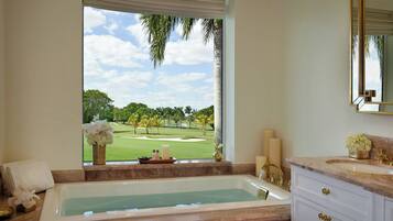 A bathroom with a bathtub, a window with a view of a golf course, and a vanity with a mirror.