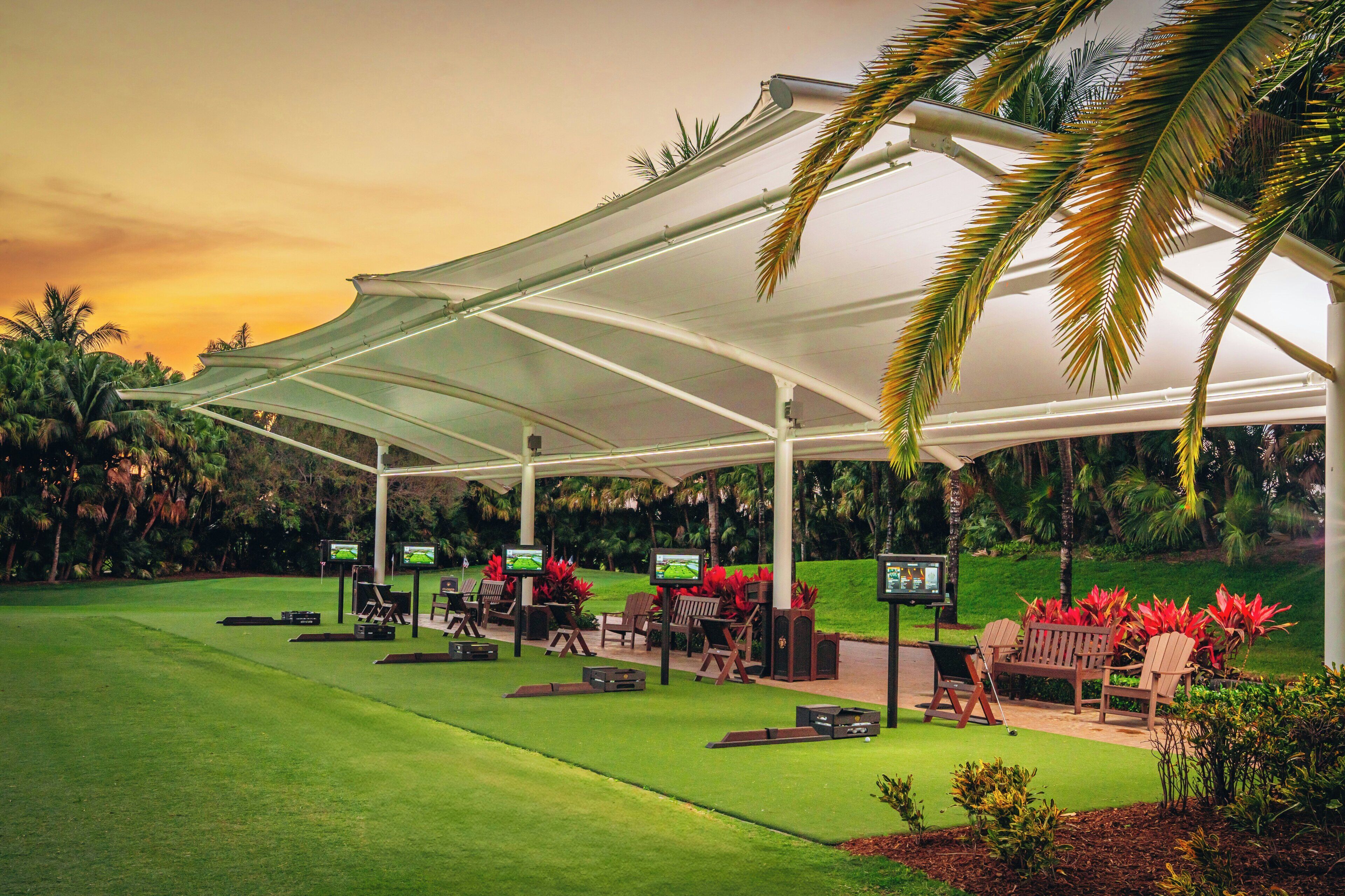 A covered outdoor area with seating and television screens, surrounded by greenery.