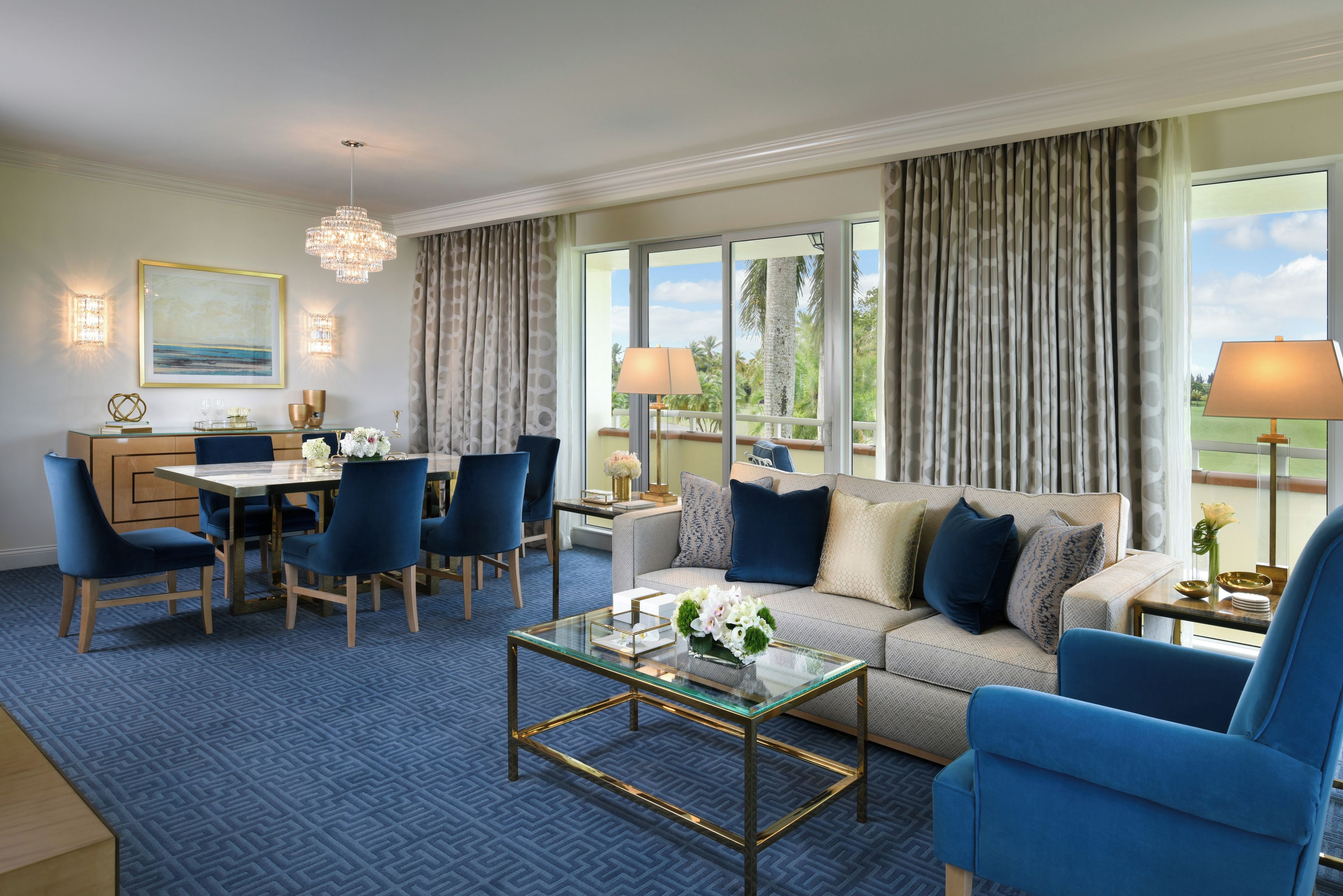 A hotel room with a dining area, a sofa, and a view of palm trees.