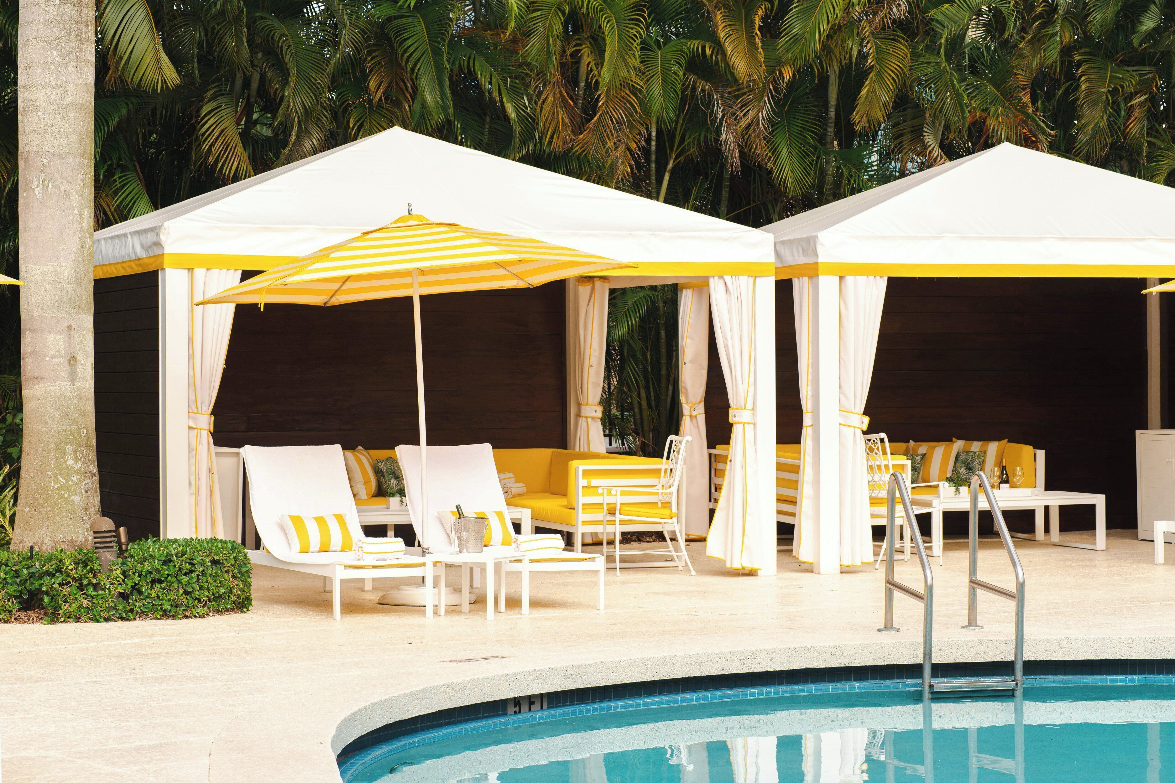 A poolside area with white canopies and yellow-striped umbrellas, lounge chairs, and a pool.