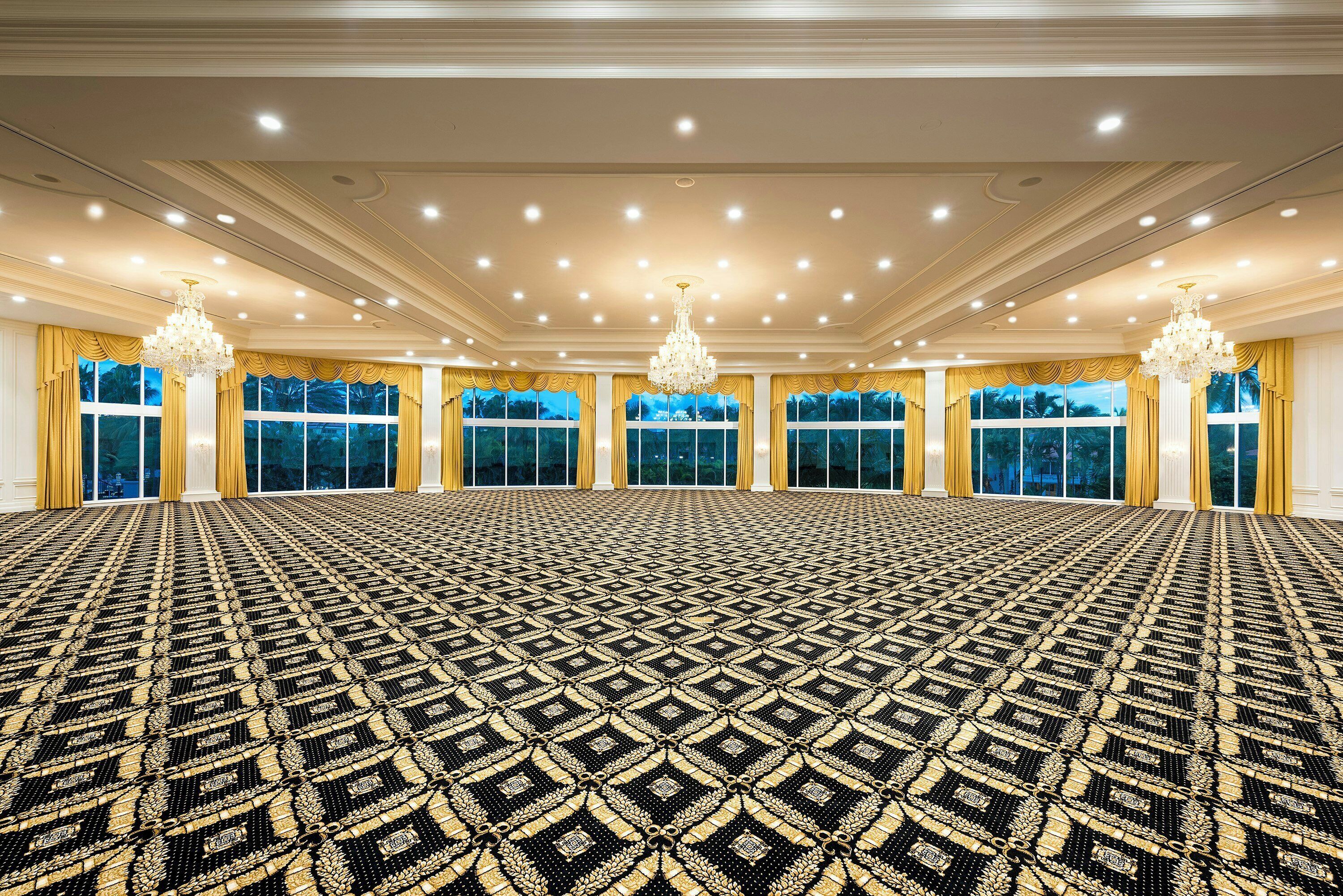 A large room with a patterned carpet, multiple windows with curtains, and chandeliers.
