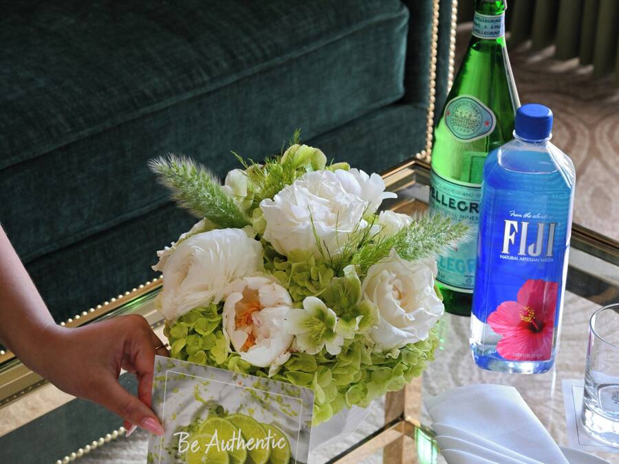 A table with a floral arrangement, a bottle of Fiji water, a glass, and a card with the text 'Be Authentic.'