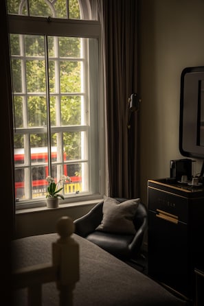 A room with a view of a red train through a window, a black leather chair, a small potted plant, and a black cabinet with a coffee maker. - Holmes Hotel London (London)