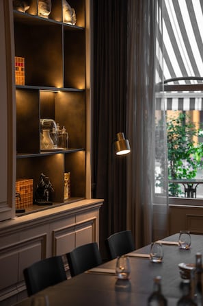 A dining area with a long table, chairs, and a shelf with decorative items. - Holmes Hotel London (London)