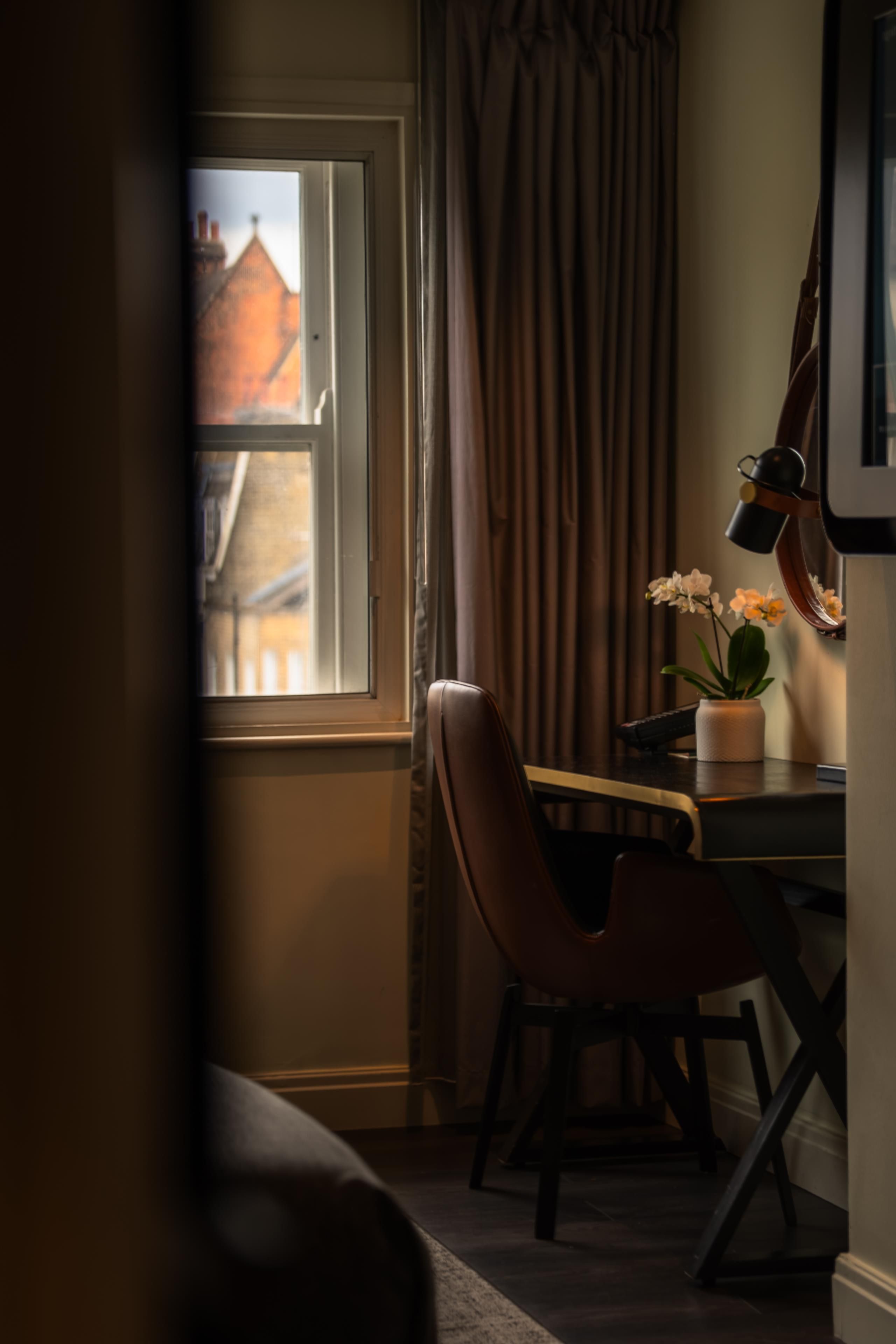 Ein Zimmer mit Esstisch, Stühlen, einer Zimmerpflanze und Blick auf Gebäude durch ein Fenster.